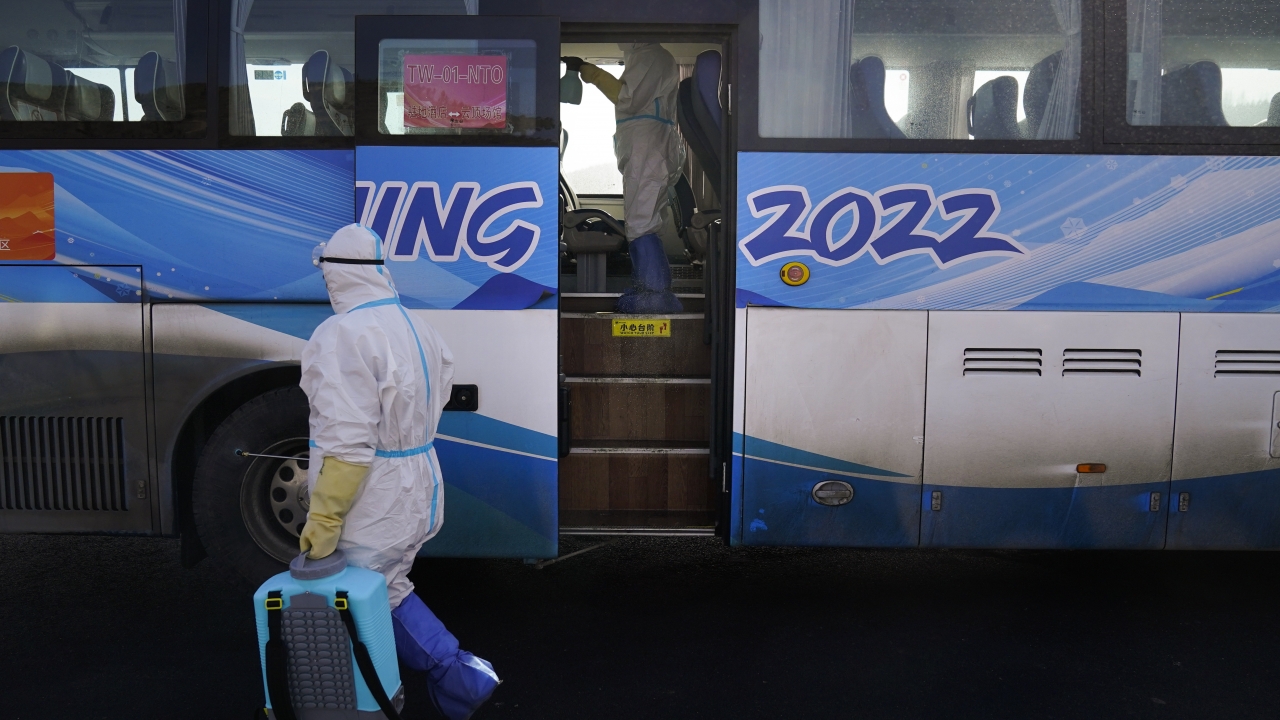 Workers in protective gear disinfect an Olympic shuttle bus.