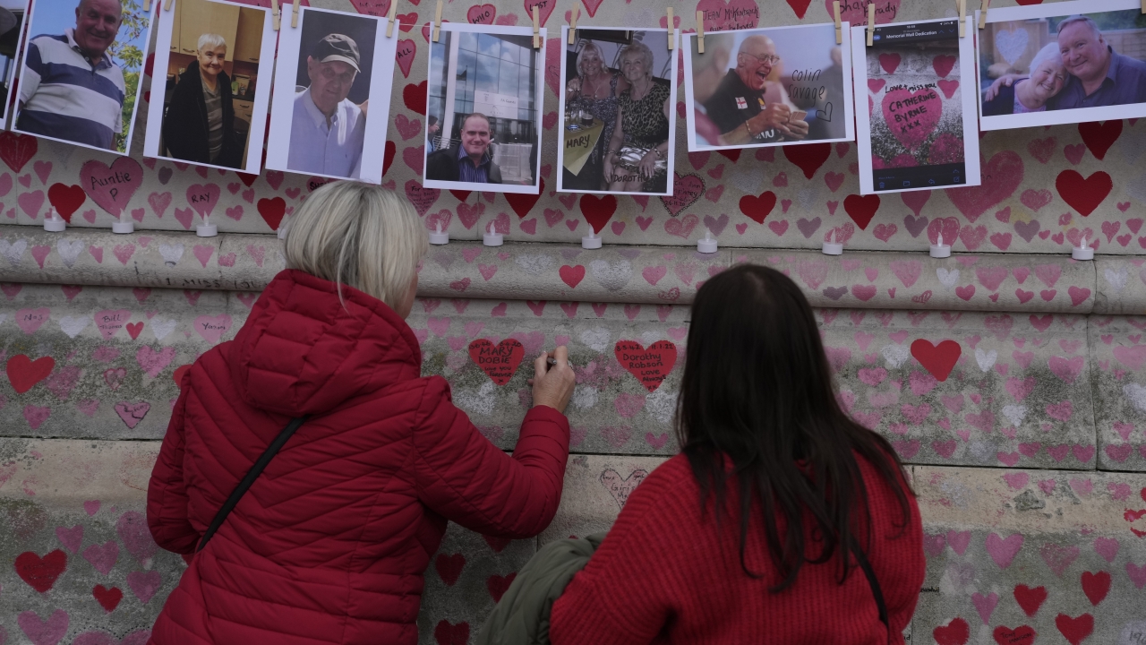 Family members write a message to two sisters who died of COVID on the National Covid Memorial wall in London
