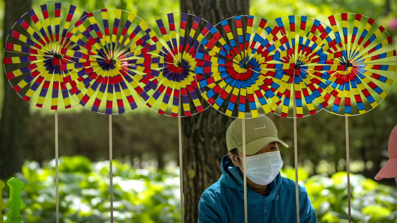 A vendor wearing a face mask sits near pinwheels for sale at a public park in Beijing