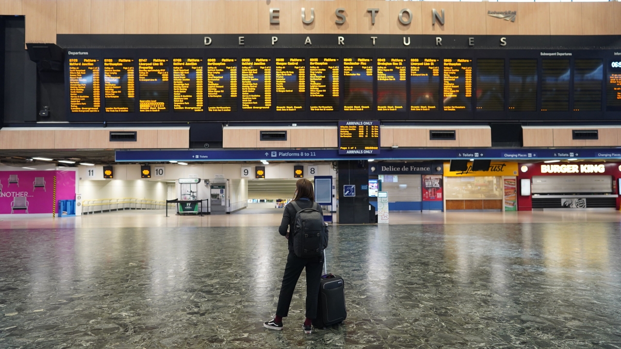 A passenger at an empty Euston station in London looks at the departures board on the first day of a rail strike