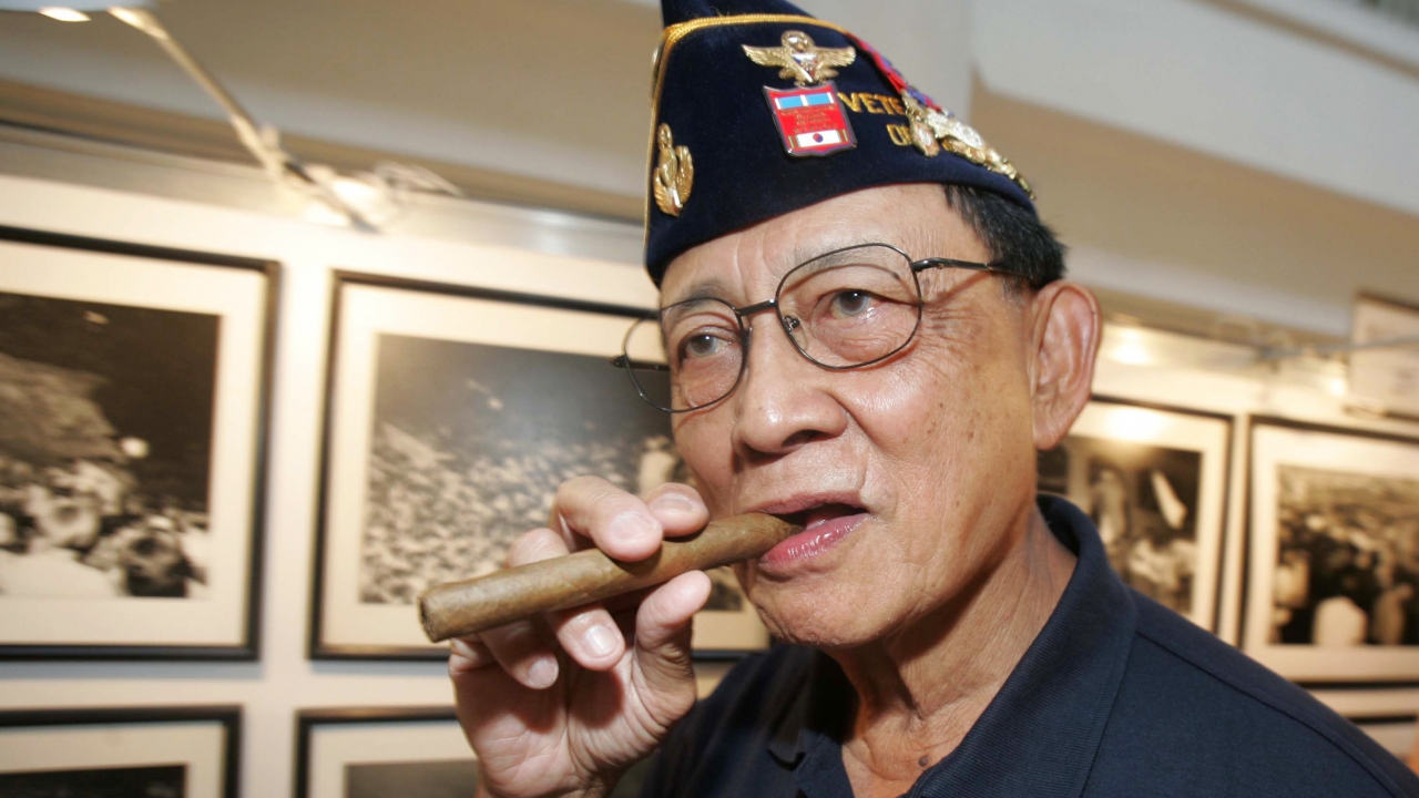 Former Philippine President Fidel Ramos bites his cigar as he looks at photographs.