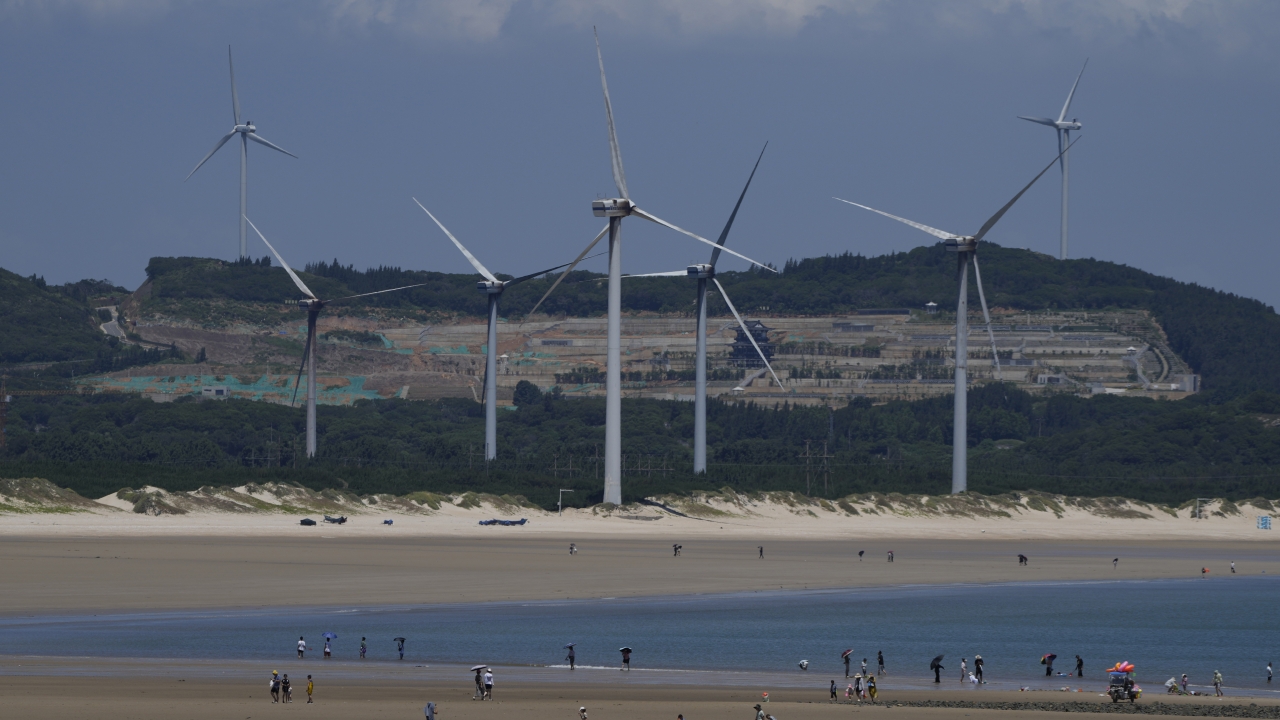 Beachgoers walk near wind turbines along the coast of Pingtan in Southern China's Fujian province