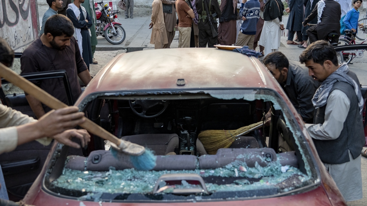 Afghan people clean a car that was damaged by an explosion.